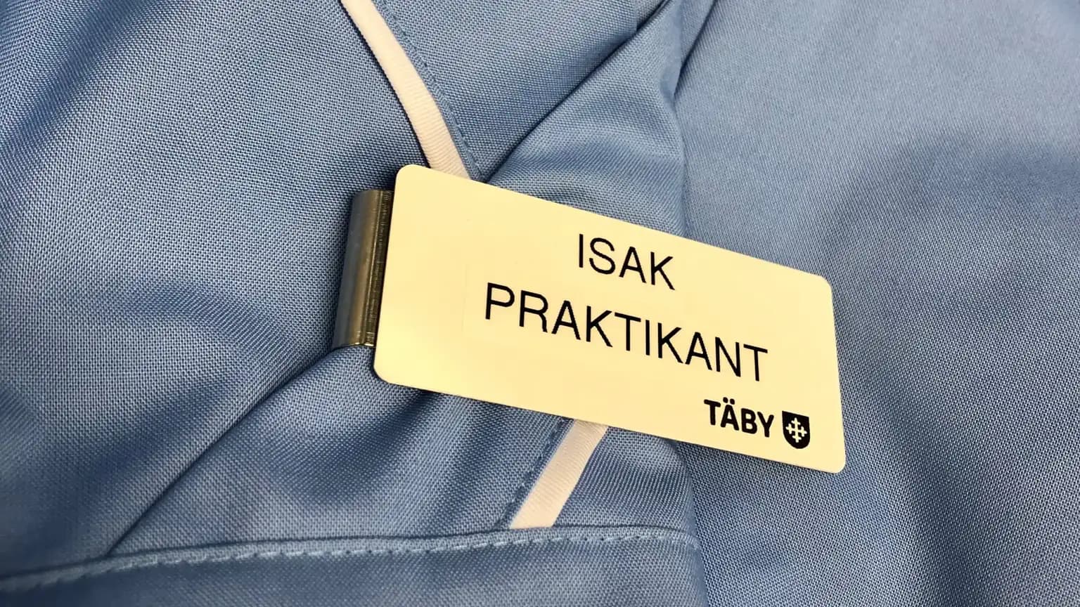 Namnskylt med texten ISAK PRAKTIKANT fäst på en ljusblå arbetsskjorta