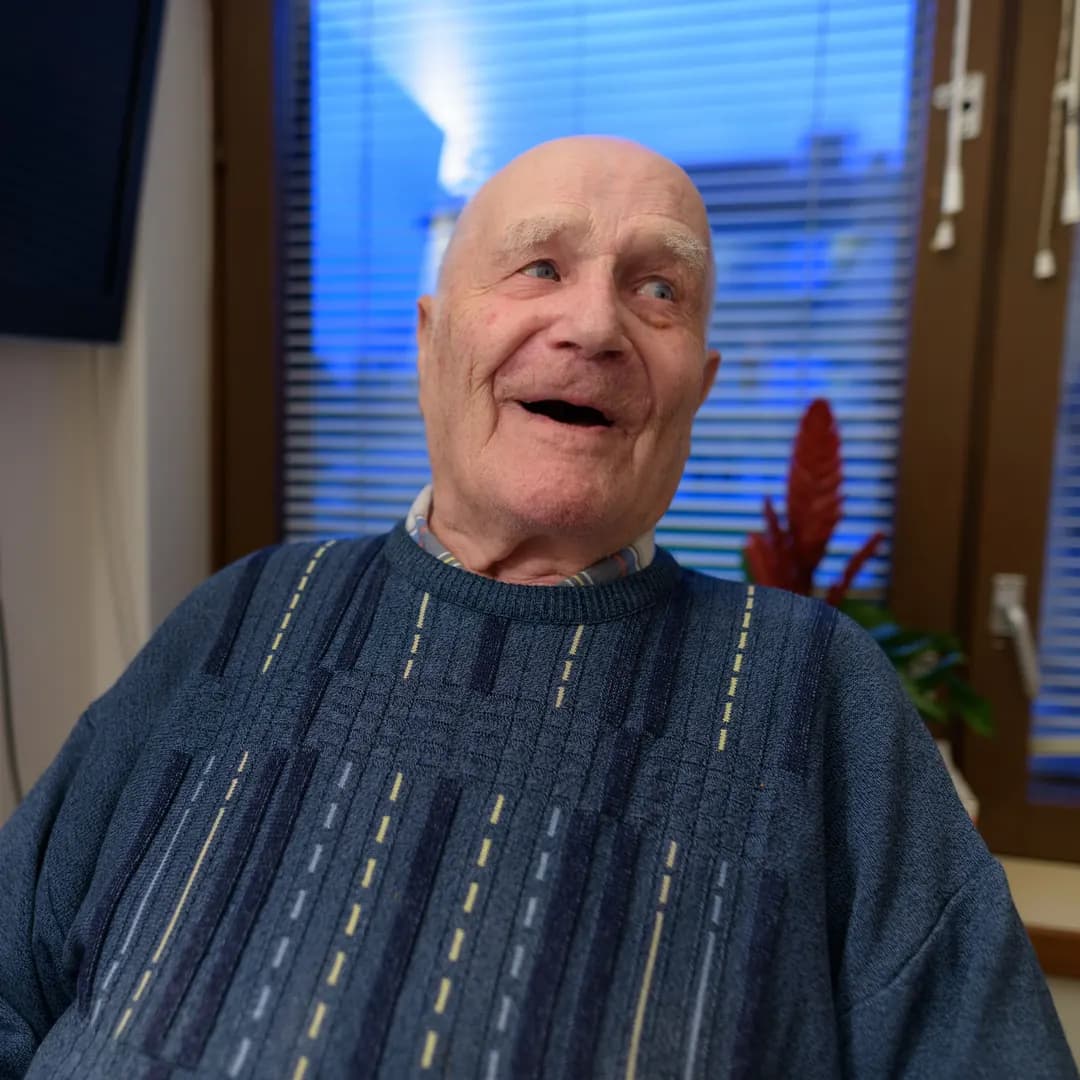 Äldre man i stickad tröja skrattar när han berättar något