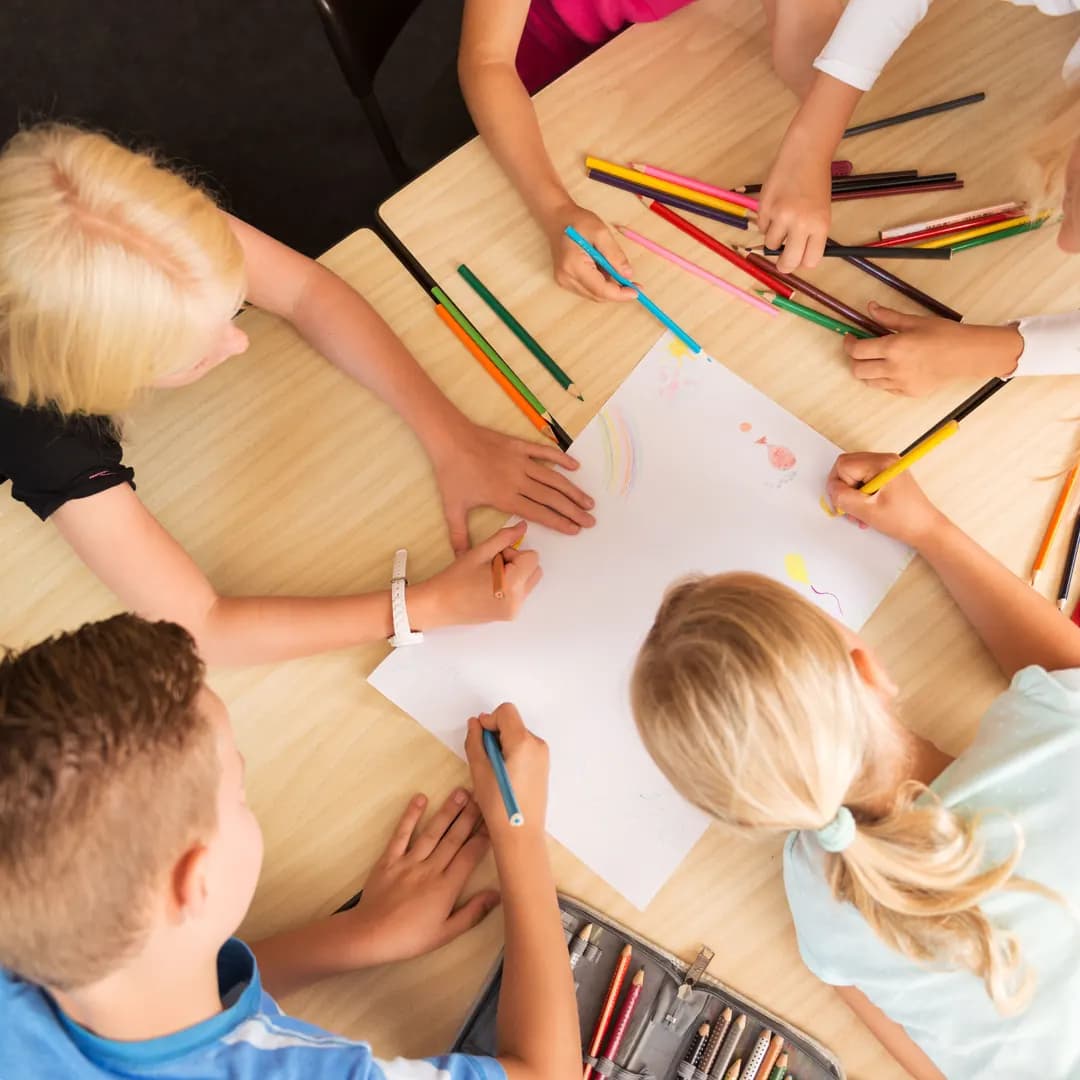 Förskolebarn ritar tillsammans runt ett bord fullt av färgpennor