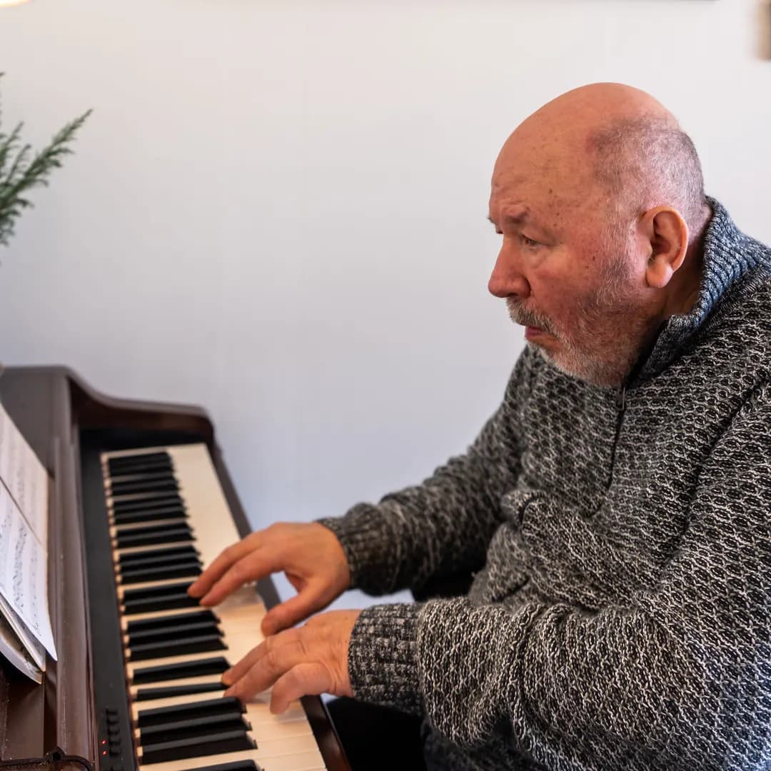 Äldre man spelar piano efter noter i ett ljust rum