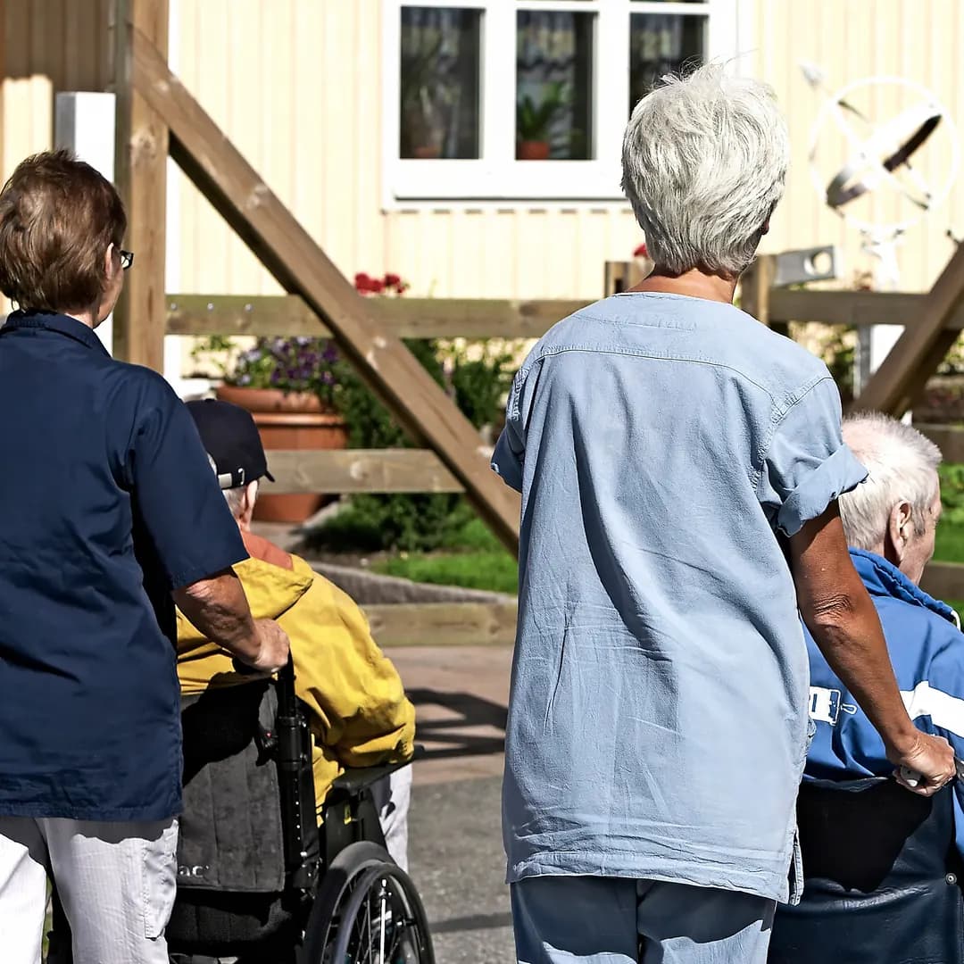 Två ur personalen tar med boende i rullstol på promenad utomhus