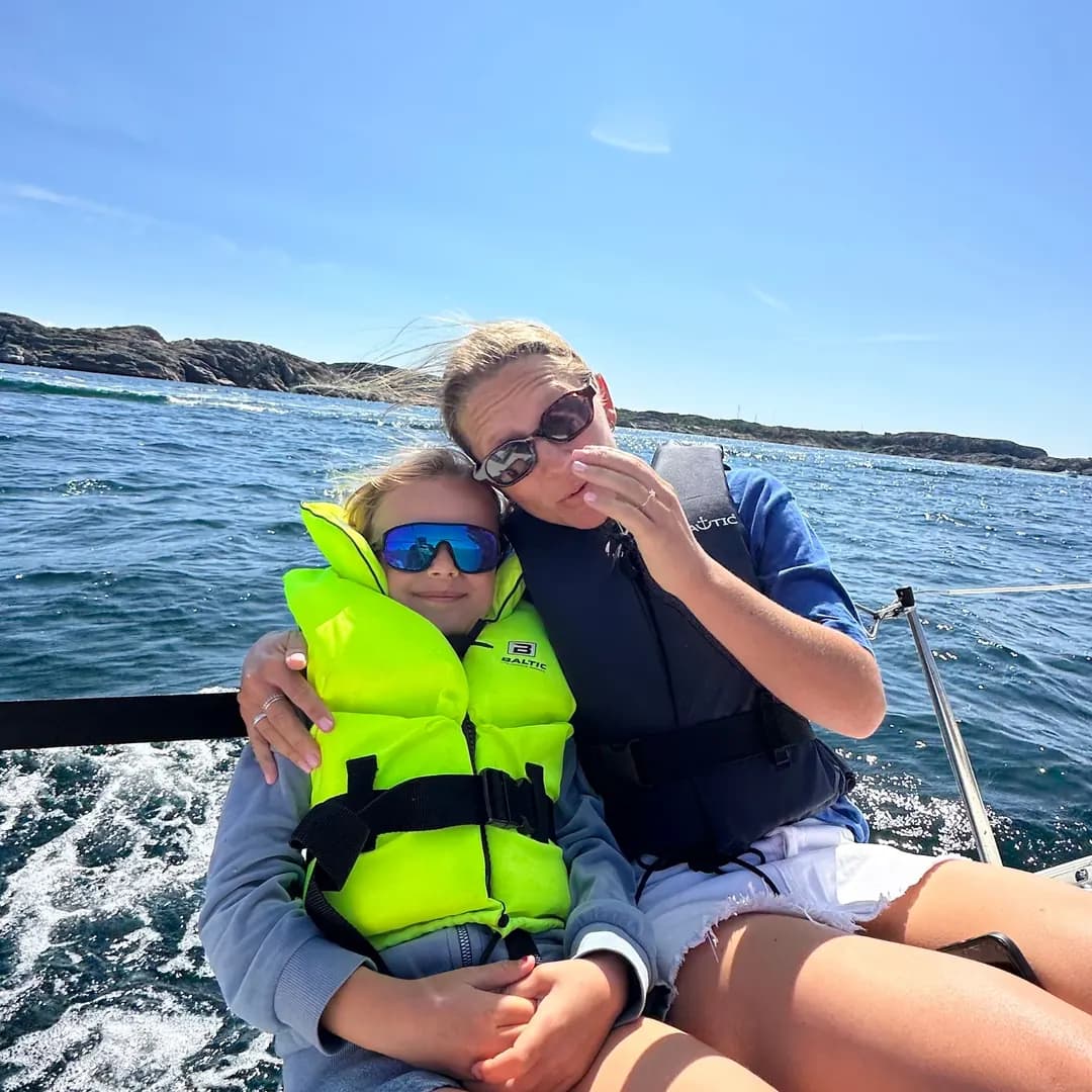 Två syskon i flytvästar sitter tätt ihop på en segelbåt ute på havet