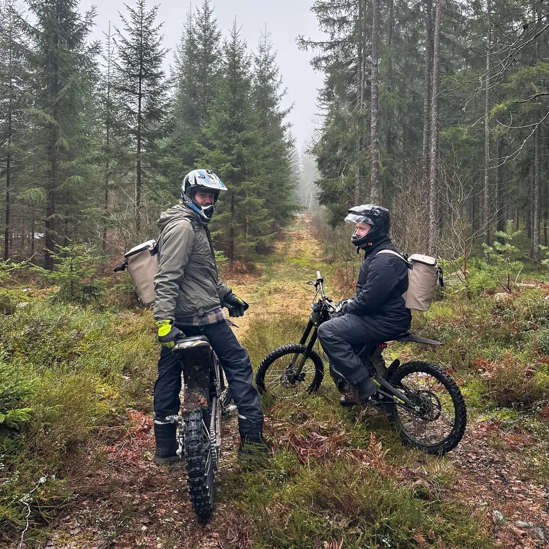 Två personer på crossmotorcyklar gör paus på en stig i en dimmig granskog